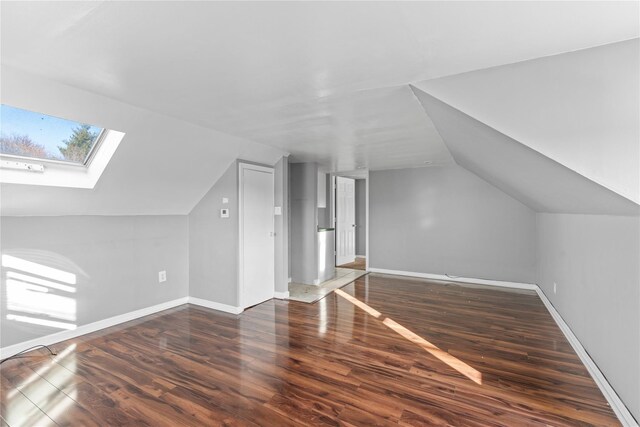 additional living space featuring vaulted ceiling with skylight and dark hardwood / wood-style floors