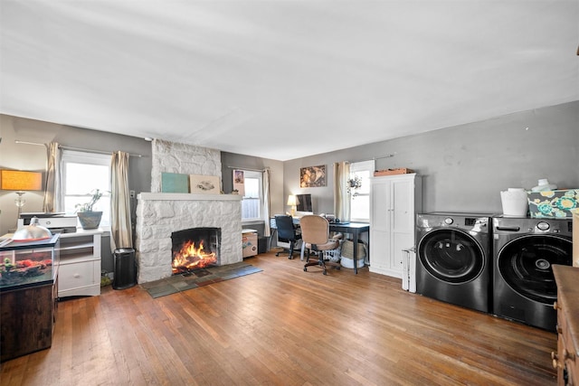 clothes washing area with independent washer and dryer, hardwood / wood-style flooring, and a stone fireplace