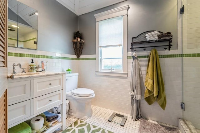bathroom featuring tile patterned flooring, toilet, vanity, a shower with shower door, and tile walls