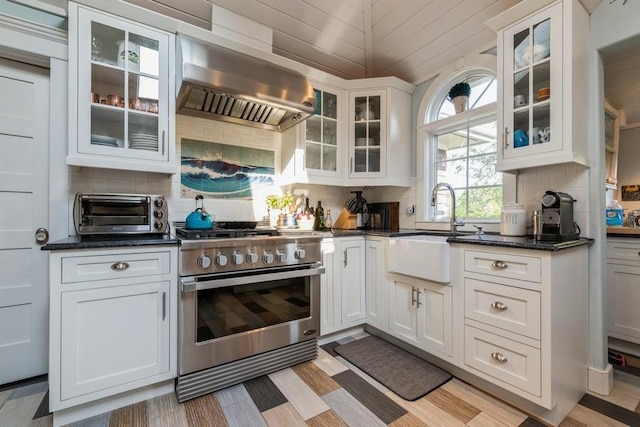 kitchen with white cabinetry, sink, wall chimney exhaust hood, high end stainless steel range oven, and dark stone countertops