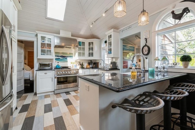 kitchen with white cabinetry, wall chimney exhaust hood, decorative light fixtures, lofted ceiling, and appliances with stainless steel finishes