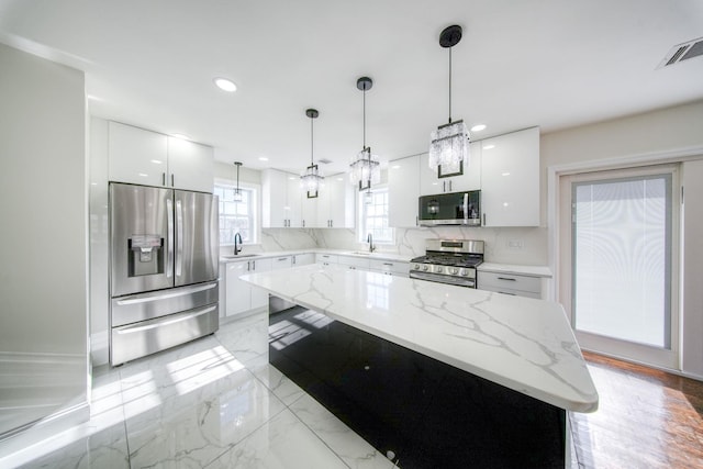 kitchen featuring a kitchen island, white cabinetry, stainless steel appliances, and hanging light fixtures