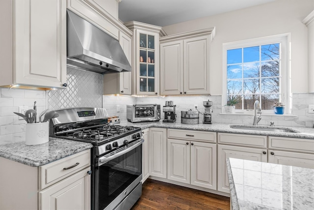 kitchen with sink, wall chimney exhaust hood, dark wood-type flooring, stainless steel gas range, and backsplash