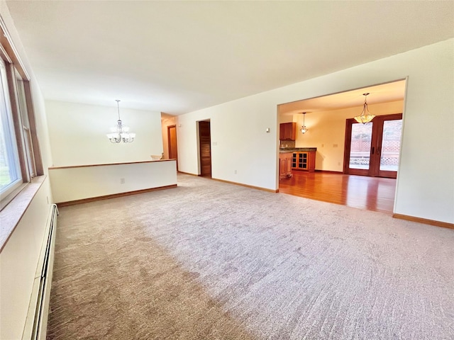 unfurnished living room with carpet flooring, a baseboard heating unit, an inviting chandelier, and a healthy amount of sunlight