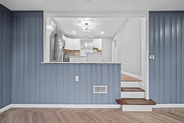kitchen featuring a peninsula, white cabinetry, visible vents, stainless steel microwave, and light countertops