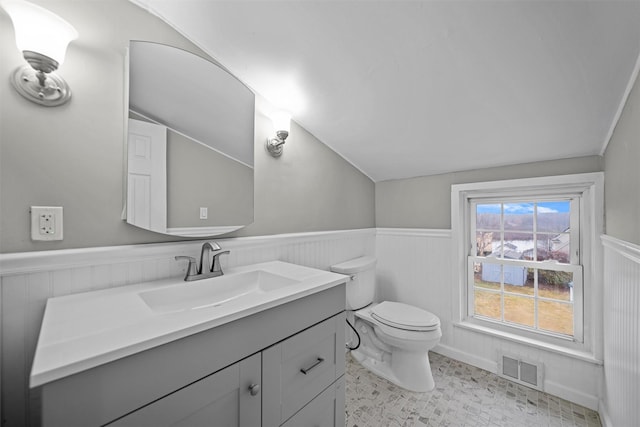 bathroom featuring visible vents, toilet, vanity, vaulted ceiling, and a wainscoted wall