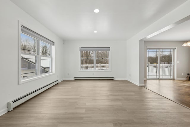 unfurnished room with a healthy amount of sunlight, a baseboard heating unit, and light hardwood / wood-style flooring