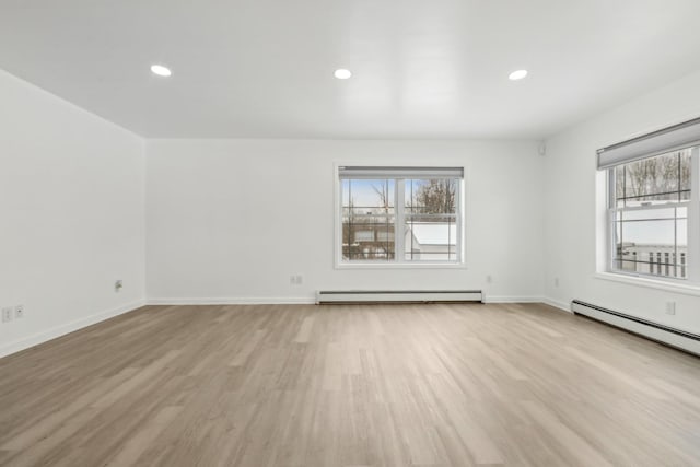 unfurnished room with baseboard heating, light wood-type flooring, and a wealth of natural light