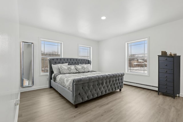 bedroom with a baseboard heating unit and light hardwood / wood-style floors