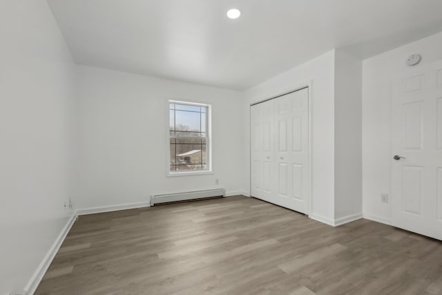 unfurnished bedroom featuring a baseboard radiator, hardwood / wood-style floors, and a closet