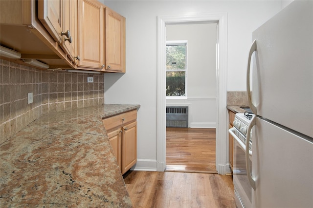 kitchen featuring radiator, tasteful backsplash, light stone counters, light hardwood / wood-style flooring, and white appliances