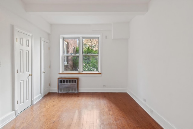 unfurnished room featuring beamed ceiling, light wood-type flooring, and radiator