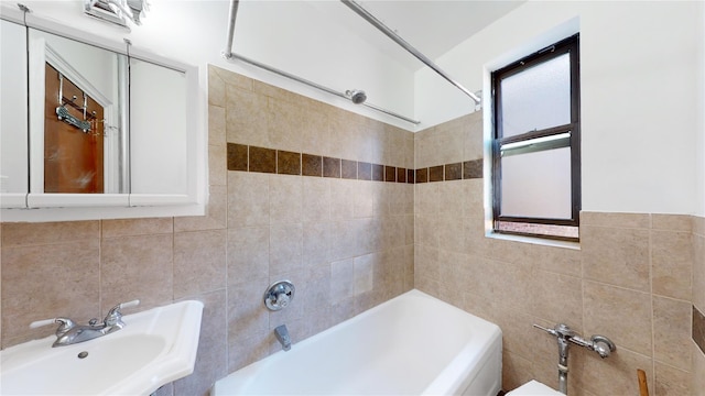 bathroom with tiled shower / bath combo, sink, and tile walls