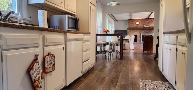 kitchen featuring white cabinets, brick wall, dark hardwood / wood-style floors, and a brick fireplace