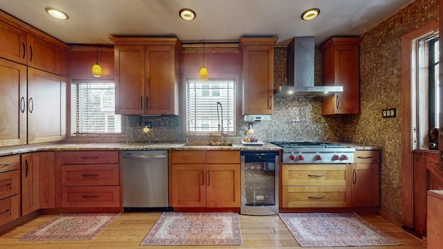 kitchen featuring stainless steel appliances, beverage cooler, wall chimney range hood, light hardwood / wood-style floors, and hanging light fixtures