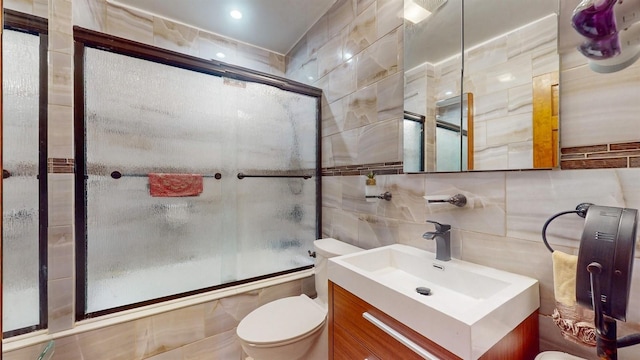 full bathroom featuring vanity, bath / shower combo with glass door, tile walls, and toilet