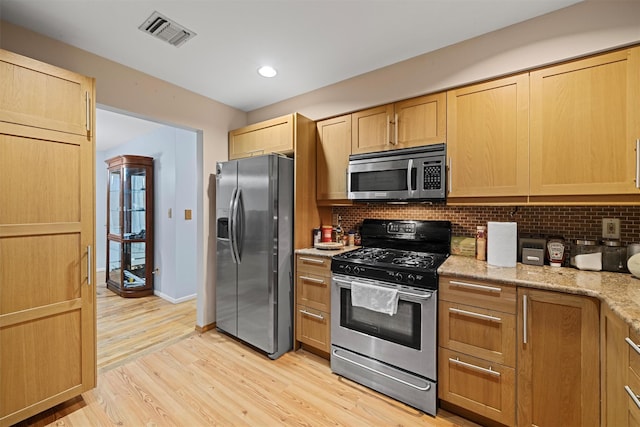 kitchen with backsplash, light stone counters, stainless steel appliances, light brown cabinets, and light hardwood / wood-style flooring