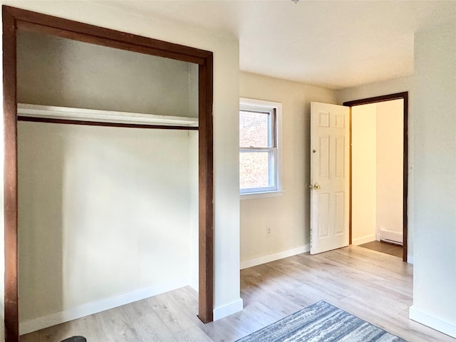 unfurnished bedroom with baseboard heating, a closet, and light hardwood / wood-style floors