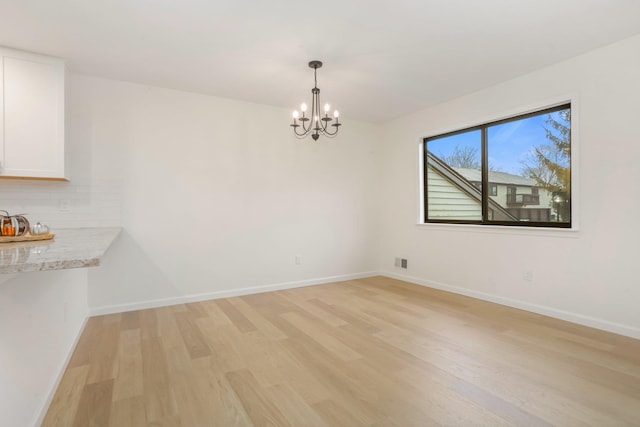 unfurnished dining area with light wood-type flooring and an inviting chandelier