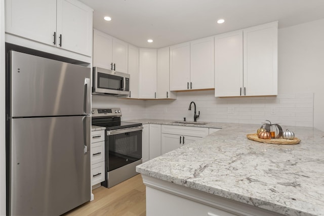 kitchen with light stone countertops, stainless steel appliances, sink, white cabinets, and light hardwood / wood-style floors