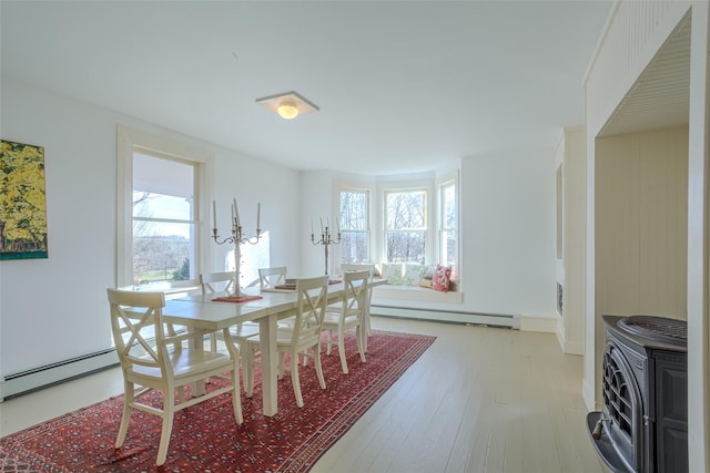 dining room with a baseboard heating unit, light wood-type flooring, a wood stove, and a healthy amount of sunlight