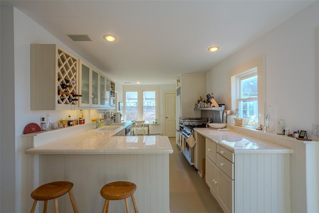 kitchen with kitchen peninsula, a kitchen breakfast bar, high end stove, sink, and tile countertops