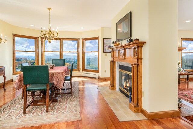 dining space with a fireplace, a baseboard radiator, a notable chandelier, and light wood-type flooring