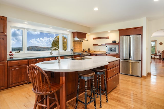 kitchen featuring a center island with sink, wall chimney exhaust hood, light hardwood / wood-style floors, a kitchen bar, and stainless steel appliances