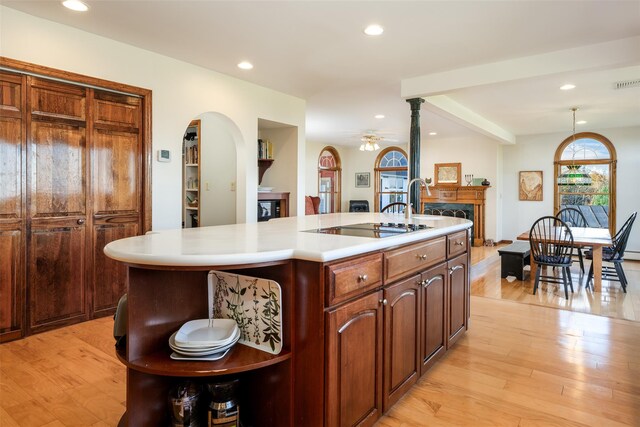 kitchen featuring ceiling fan, a center island with sink, light hardwood / wood-style floors, hanging light fixtures, and black stovetop