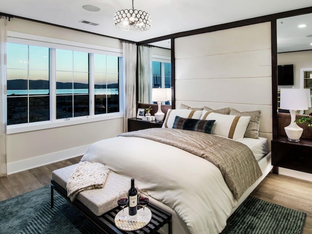 bedroom with a water view, wood-type flooring, and an inviting chandelier