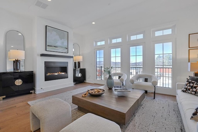 living room with recessed lighting, visible vents, light wood-style flooring, a glass covered fireplace, and baseboards