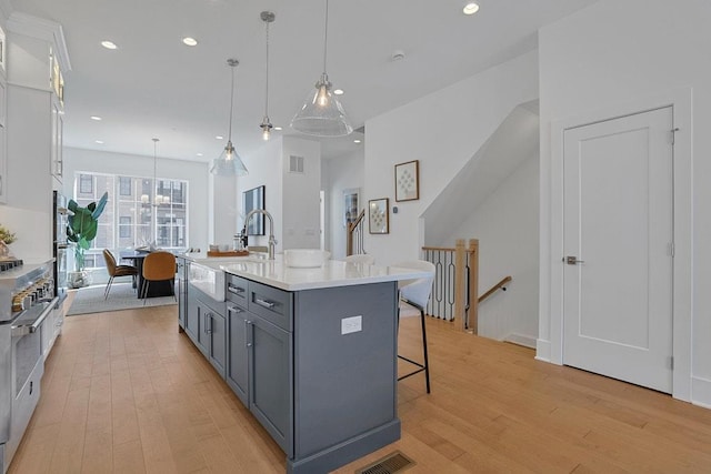 kitchen with gray cabinets, a kitchen island with sink, white cabinets, and light countertops