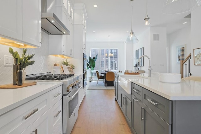 kitchen with stainless steel stove, visible vents, light countertops, an island with sink, and decorative light fixtures