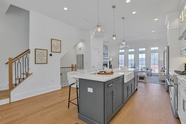 kitchen featuring an island with sink, open floor plan, light countertops, gray cabinetry, and white cabinetry