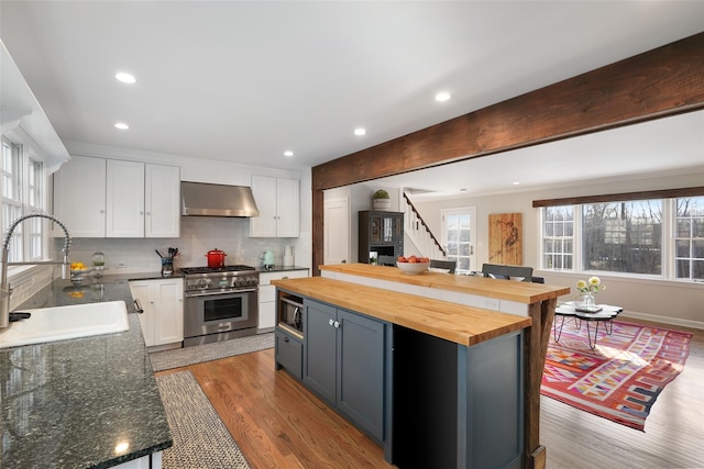 kitchen with butcher block countertops, a sink, ventilation hood, high end stainless steel range oven, and built in microwave