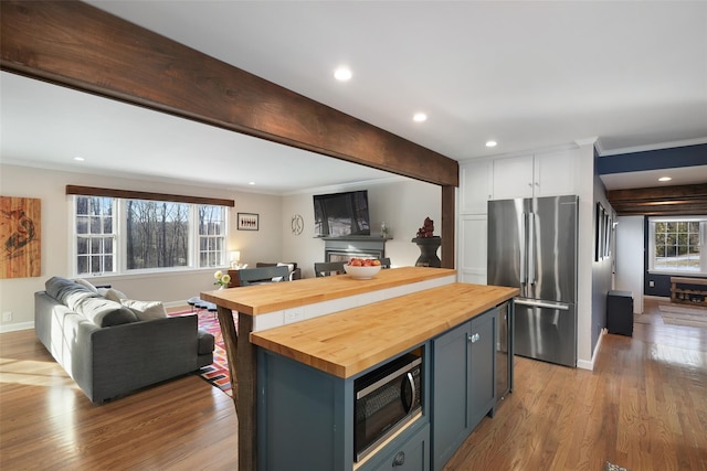 kitchen featuring wood counters, freestanding refrigerator, built in microwave, white cabinetry, and beam ceiling