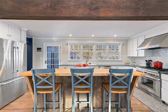 kitchen featuring stainless steel appliances, white cabinets, wooden counters, wall chimney range hood, and light wood-type flooring