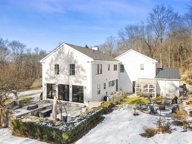 snow covered back of property featuring metal roof, an outdoor fire pit, cooling unit, a garage, and an outdoor structure