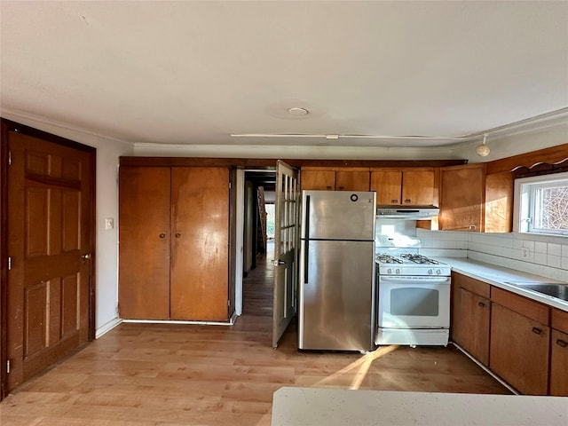 kitchen featuring decorative backsplash, gas range gas stove, sink, light hardwood / wood-style flooring, and stainless steel refrigerator