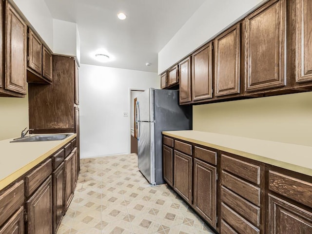 kitchen featuring stainless steel refrigerator, dark brown cabinetry, and sink