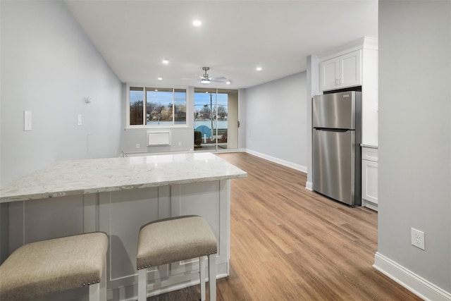 kitchen with stainless steel refrigerator, light stone countertops, light hardwood / wood-style floors, a kitchen bar, and white cabinets