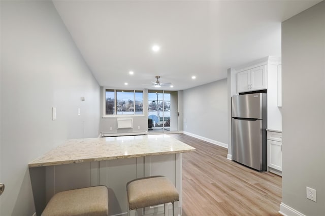 kitchen with light wood-style floors, freestanding refrigerator, a peninsula, white cabinets, and light stone counters