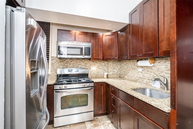 kitchen with light stone countertops, backsplash, stainless steel appliances, and sink