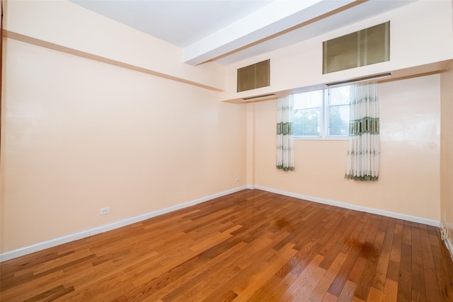 spare room with beam ceiling and wood-type flooring