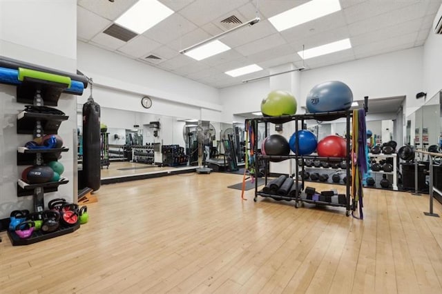 gym with a towering ceiling, a paneled ceiling, and light hardwood / wood-style flooring