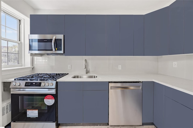 kitchen featuring appliances with stainless steel finishes, light stone counters, radiator, sink, and blue cabinetry