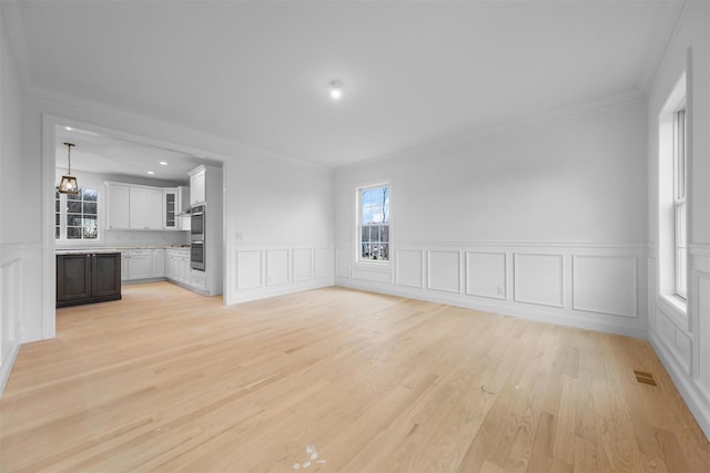 unfurnished living room featuring light wood-type flooring and ornamental molding