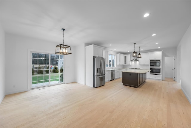 kitchen featuring white cabinetry, a center island, stainless steel appliances, pendant lighting, and light wood-type flooring