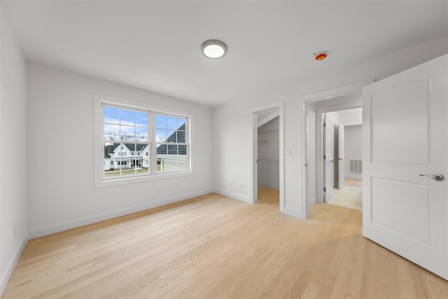 unfurnished bedroom with light wood-type flooring, a spacious closet, and a closet