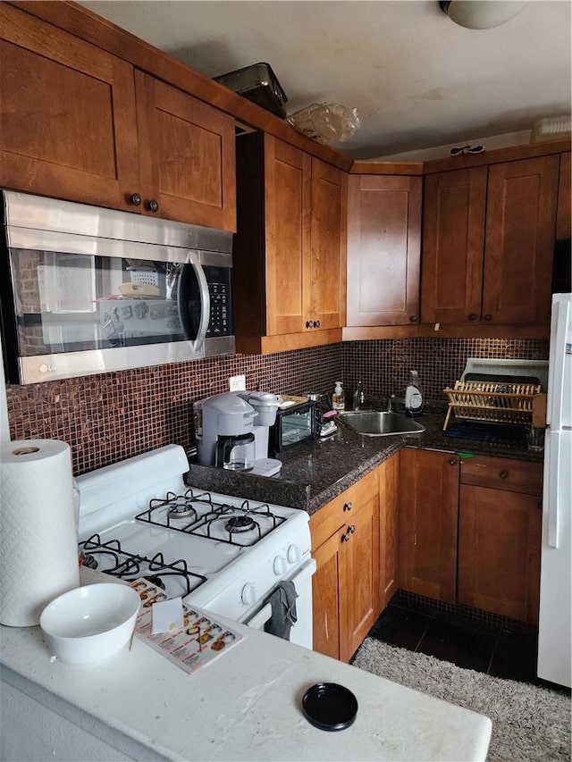 kitchen with sink, tasteful backsplash, dark stone countertops, white appliances, and light tile patterned floors